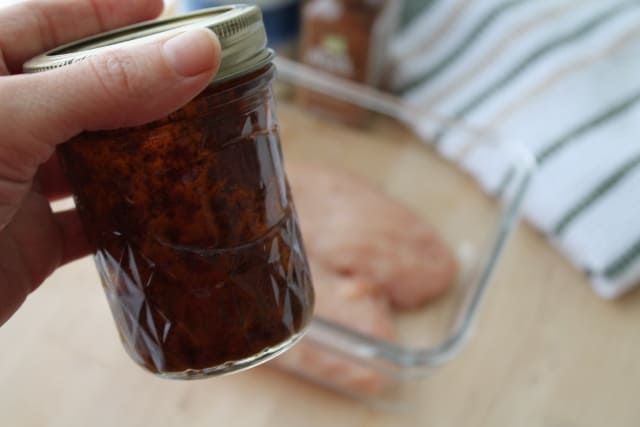 A hand holding a jar of marinade.