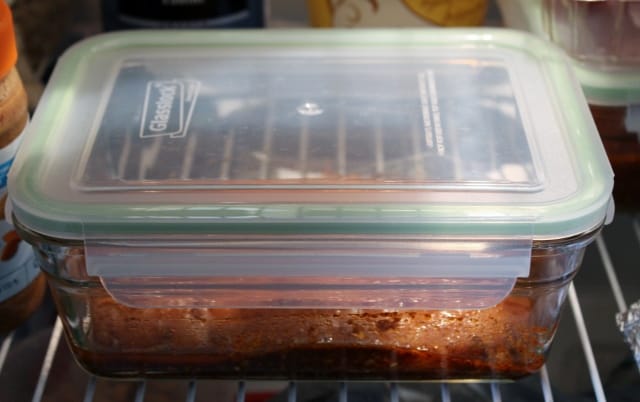 Meat marinating in a glass container in the fridge.