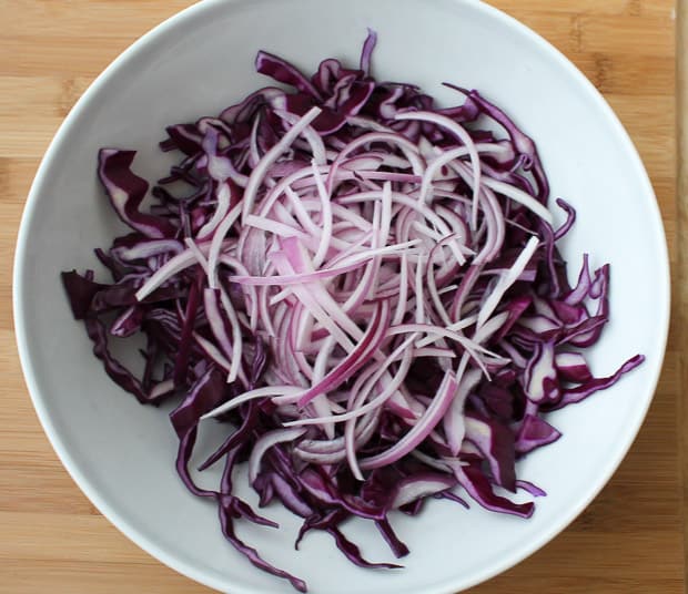 shredded red cabbage in a large mixing bowl topped with sliced onions