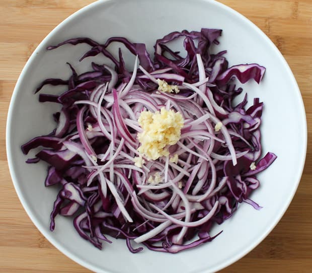 shredded red cabbage in a large mixing bowl topped with sliced onions and minced garlic