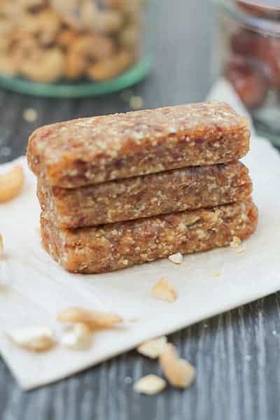 Homemade Cashew Cookie Larabar sitting on a piece of parchment paper with cashew pieces and dates in a jar