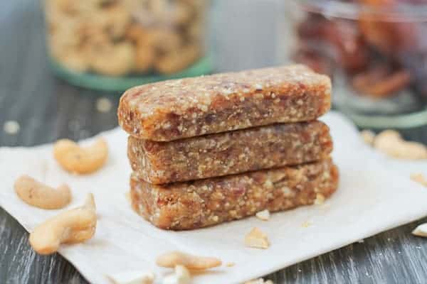 Date bars sitting on parchment paper with cashews and dates in jars in the background