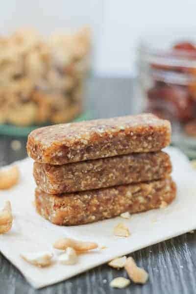 Date Bars on parchment paper with jars of cashews and dates in the background.