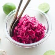 Garlic Lime Red Cabbage Slaw in a bowl with fresh cut limes and garlic cloves in the background