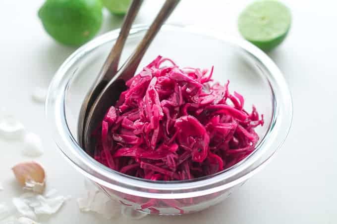 Garlic Lime Red Cabbage Slaw in a bowl with fresh limes in the background