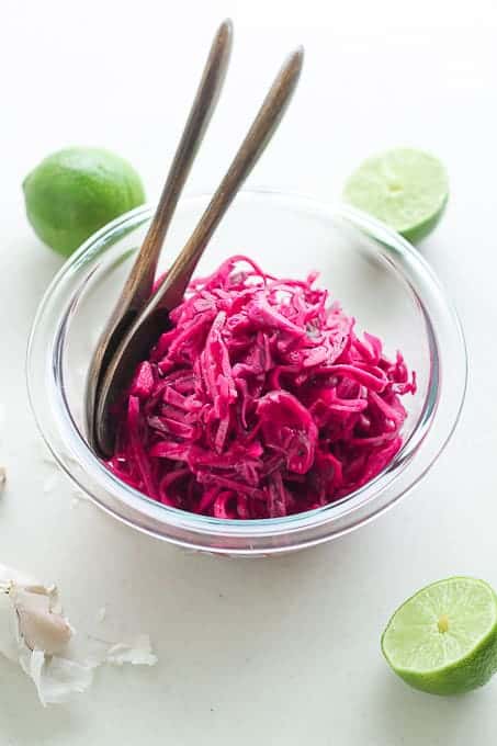 Garlic Lime Red Cabbage Slaw in a bowl with fresh cut limes and garlic cloves in the background