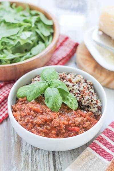 Quinoa & Bolognese Sauce garnished with fresh basil and an arugula salad in a wooden bowl