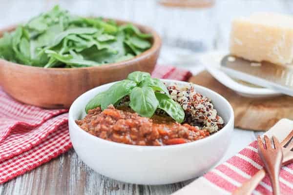 Quinoa & Bolognese Sauce garnished with fresh basil and an arugula salad in a wooden bowl