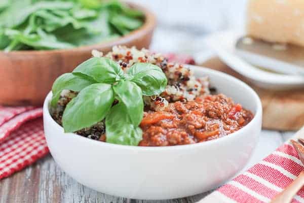 Quinoa & Bolognese Sauce garnished with fresh basil and an arugula salad in a wooden bowl