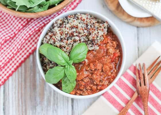Quinoa & Bolognese Sauce garnished with fresh basil and an arugula salad in a wooden bowl