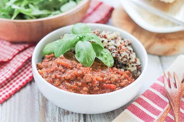 Quinoa & Bolognese Sauce garnished with fresh basil and an arugula salad in a wooden bowl