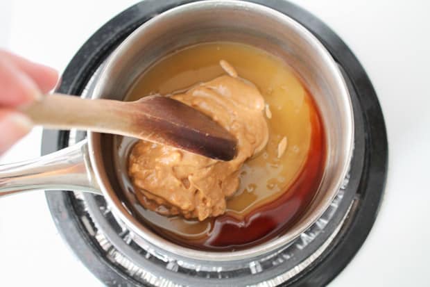 A small saucepan with peanut butter and brown rice syrup being mixed together with a wooden spoon.