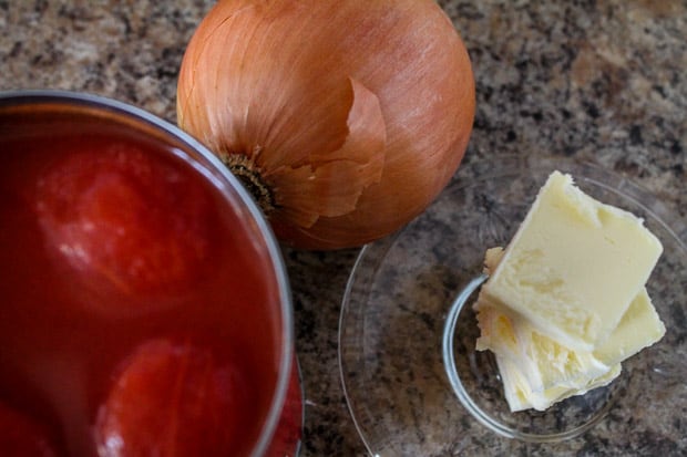 A can of plum tomatoes with an onion and a few pats of butter on a counter 