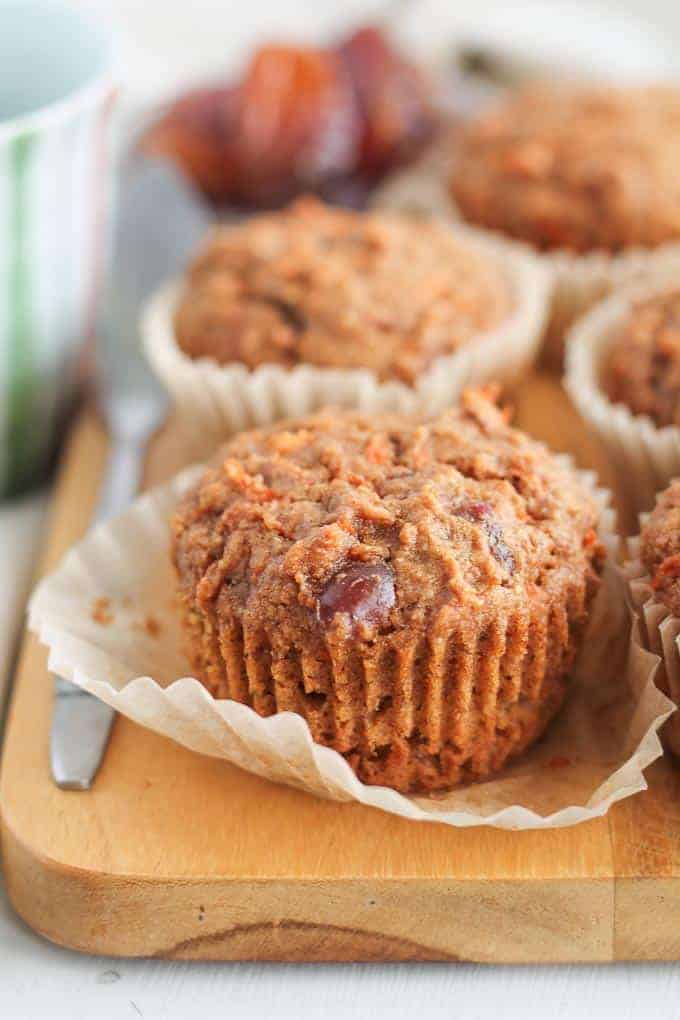 Freshly baked Carrot Date Muffins on a wooden board with a cup of coffee in the background