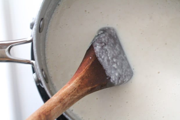 a spoon stirring white sauce in a saucepan.