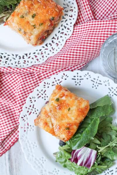 Cheesy casserole on a plate with a side salad and red checkered napkin.