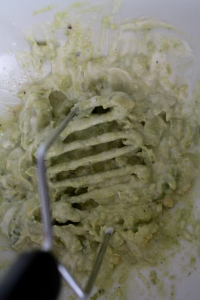 avocado being combined with Greek yogurt by a potato masher