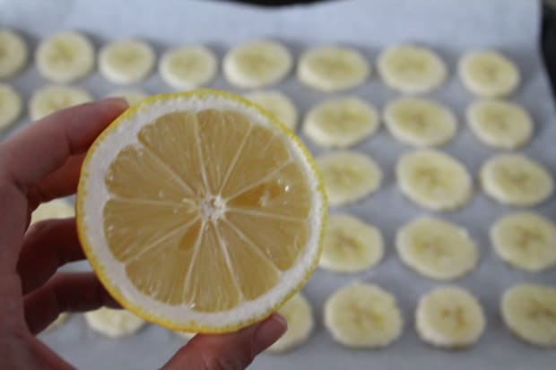 A lemon being squeezed over sliced bananas on a baking sheet