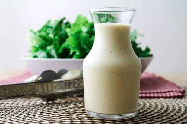  Vegan Caesar Salad Dressing in a container with a bowl of salad greens in the background