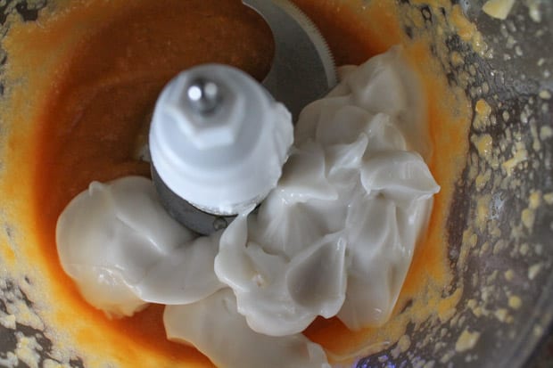 coconut yogurt being added to a food processor with pureed peaches