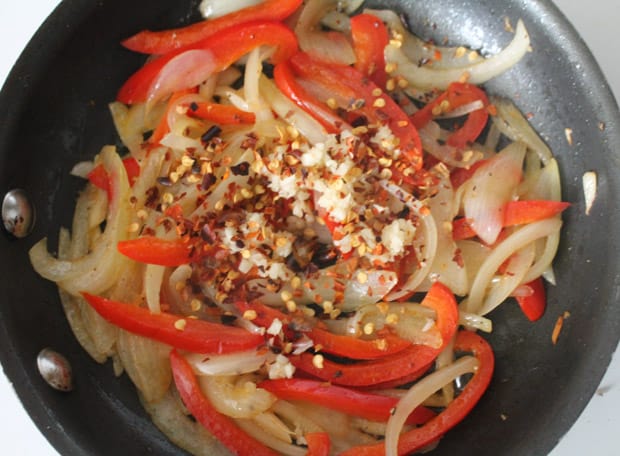 onions and peppers sauteed in a pan with chili flakes on top