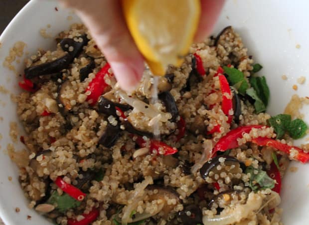 A hand squeezing lemon into a bowl of eggplant quinoa salad