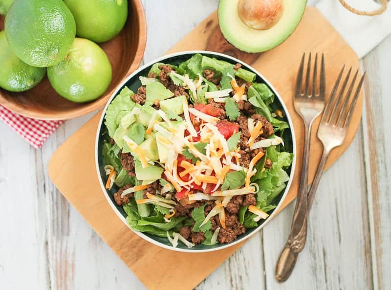 layered healthy taco salad in a bowl with fresh limes and avocado in the background