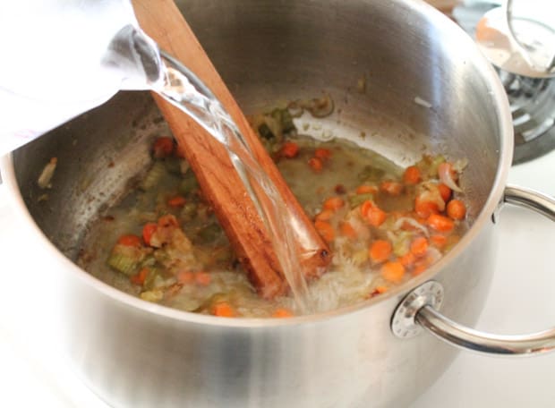 water being poured over sauteed vegetables in a soup pot