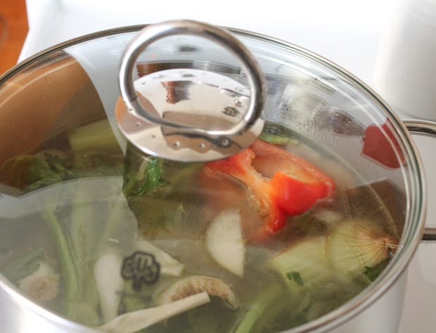 a soup pot full of veggies and water with a glass lid covering it