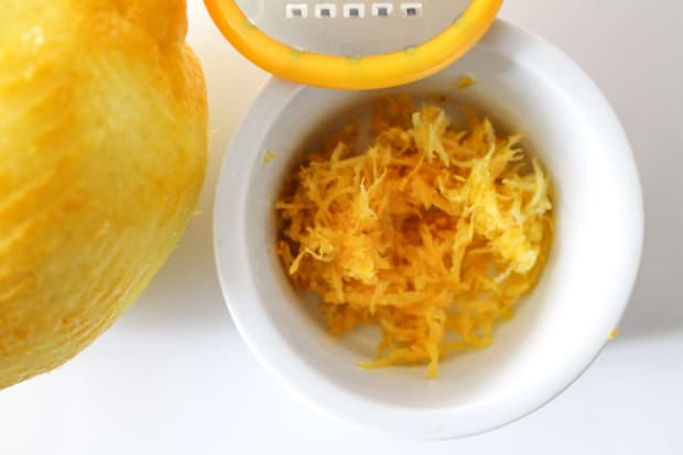 lemon zest in a white ramekin with a zested lemon and zesting tool in the background