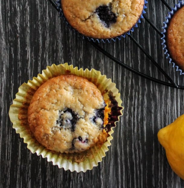 Fresh baked Lemon Berry Quinoa Flour Muffins on a wooden surface with a lemon in the background