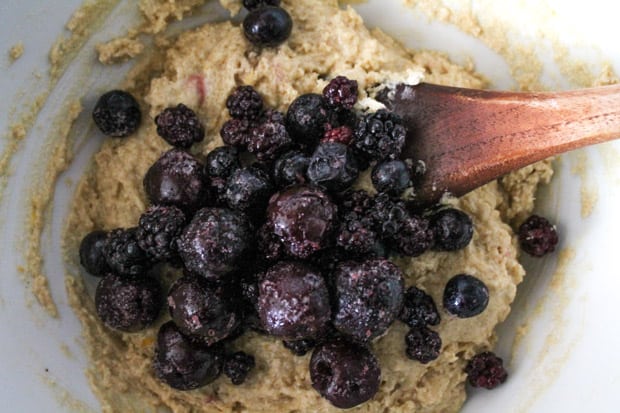 frozen berries being stirred into muffin batter by a wooden spoon