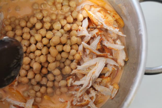 chicken and chickpeas being added to a soup pot