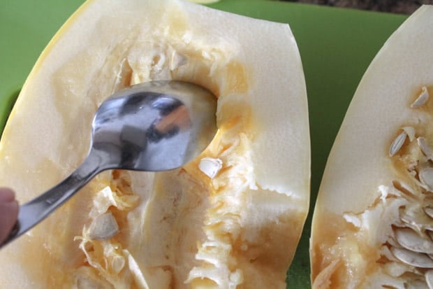 a spoon scraping out seeds from a squash.