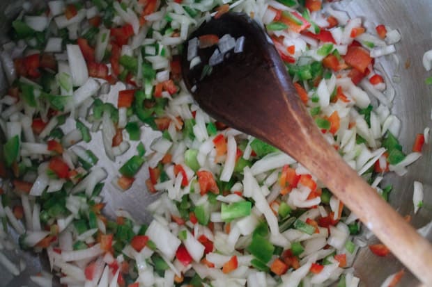 a wooden spoon stirring diced veggies in a big pot