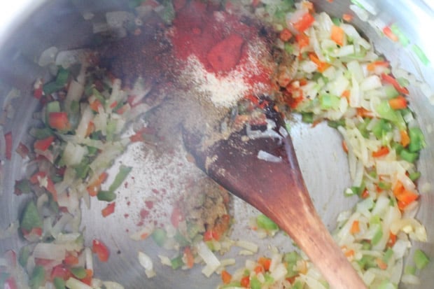a wooden spoon stirring spices into diced sauteed veggies