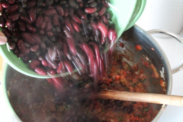 beans being poured into a big pot of chili