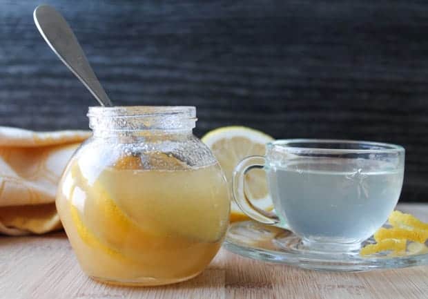 Natural Honey Lemon Cold Remedy in a jar with a mug of hot water in the background