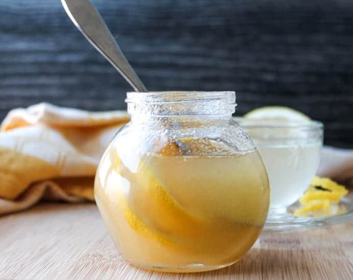 Natural Honey Lemon Cold Remedy in a jar with a mug of hot water in the background