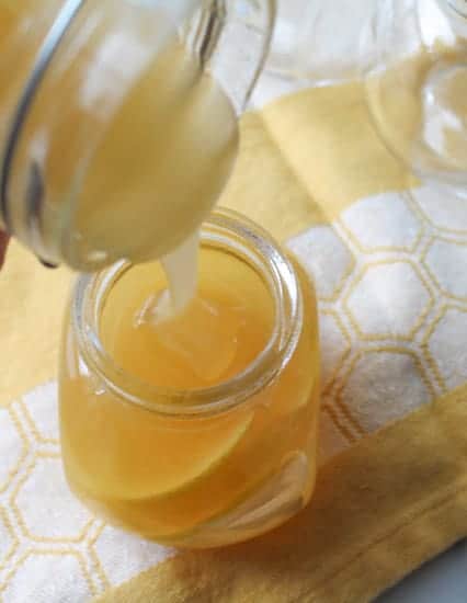 honey being poured into a glass jar over sliced lemons