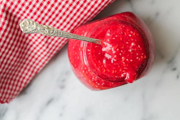 Raspberry chia seed jam in a jar sitting on a a marble surface with a red checkered napkin in the background