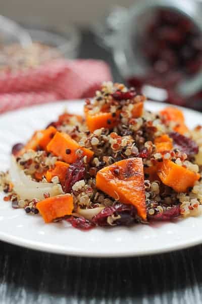 Spicy Roasted Butternut Squash with Quinoa & Cranberries on a white plate with a red checkered napkin in the background