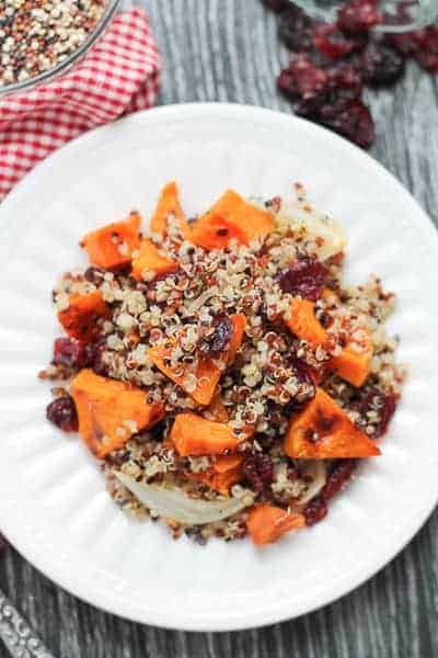 Spicy Roasted Butternut Squash with Quinoa & Cranberries on a white plate with a red checkered napkin in the background