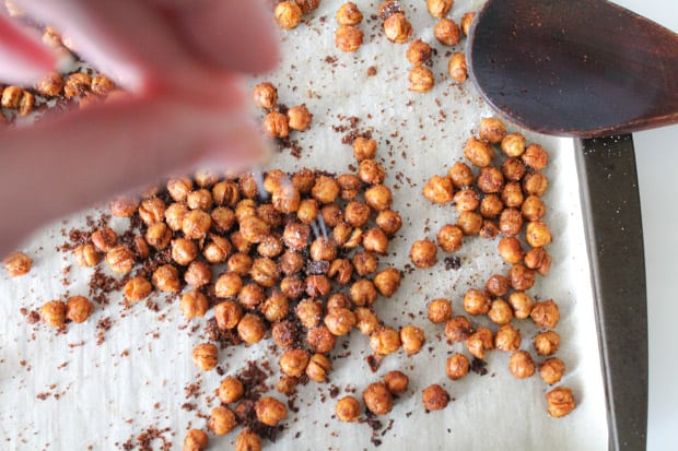 Spicy roasted chickpeas being seasoned on a baking sheet
