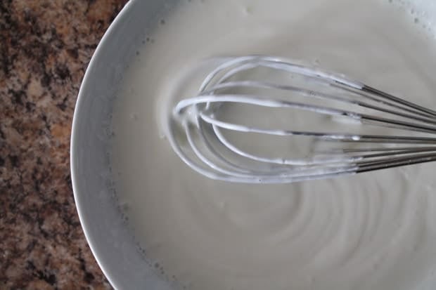 a whisk stirring together greek yogurt and milk in a white mixing bowl