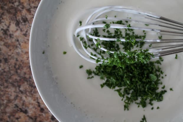 freshly chopped parsley being added to a mixture of greek yogurt and milk