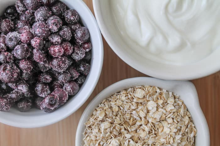 frozen berries, Greek yogurt and oats in measuring cups on a wooden background.
