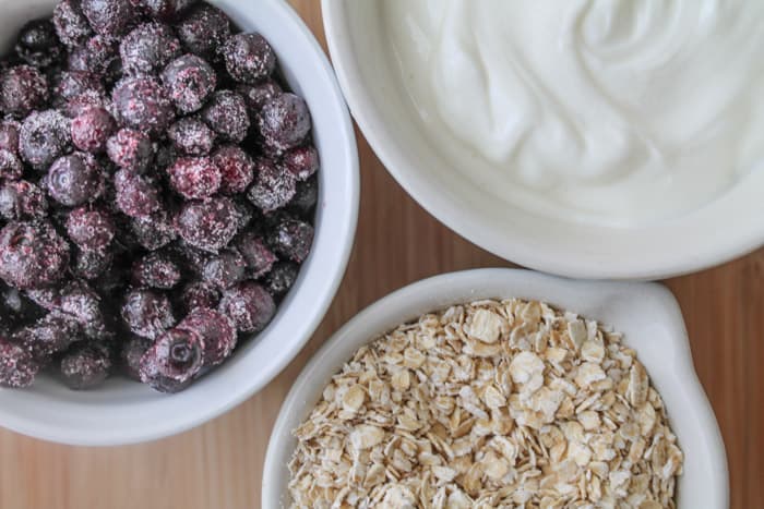 Blueberry Breakfast Smoothie frozen berries, Greek yogurt and oats in measuring cups on a wooden background.