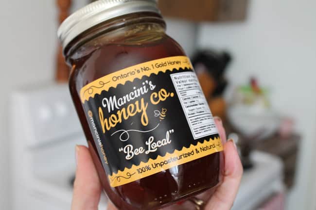 A hand holding a jar of local honey with a black and yellow lable