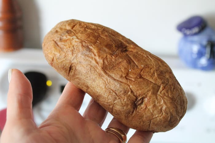 A hand holding a leftover baked potato